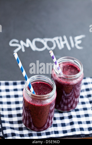 Heidelbeere Smoothies in Gläsern mit Strohhalmen auf karierte Serviette mit Kreide auf dunklem Hintergrund geschriebene Wort-smoothie Stockfoto