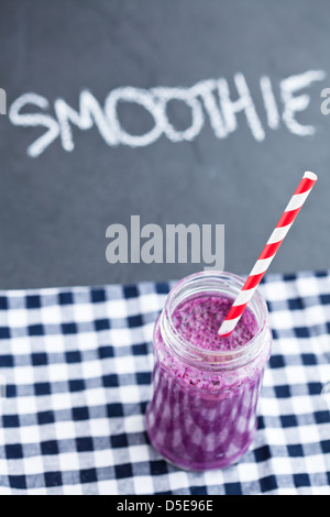 Blueberry Smoothie im Glas mit Strohhalm auf karierte Serviette mit Kreide auf dunklem Hintergrund geschriebene Wort-smoothie Stockfoto
