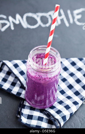 Blueberry Smoothie im Glas mit Strohhalm auf karierte Serviette mit Kreide auf dunklem Hintergrund geschriebene Wort-smoothie Stockfoto