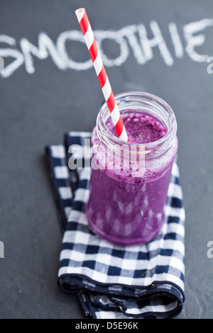 Blueberry Smoothie im Glas mit Strohhalm auf karierte Serviette mit Kreide auf dunklem Hintergrund geschriebene Wort-smoothie Stockfoto