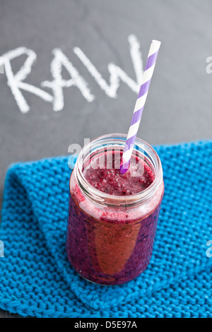 Nahaufnahme von Blueberry Smoothie aus Glas mit gestreiften Stroh ruht auf blauen Matte mit rohen Wort geschrieben in Kreide auf Hintergrund Stockfoto