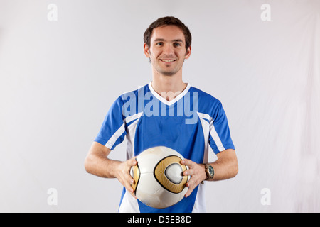 Hübscher junger Mann im Fußball Uniform, halten einen Fußball und lächelt in die Kamera Stockfoto