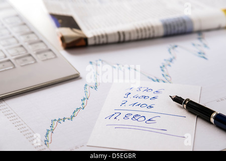 Nahaufnahme von Rechner, Wirtschaftszeitung, Diagramm und habe mit Stift Euro Werte aufgeschrieben. Stockfoto