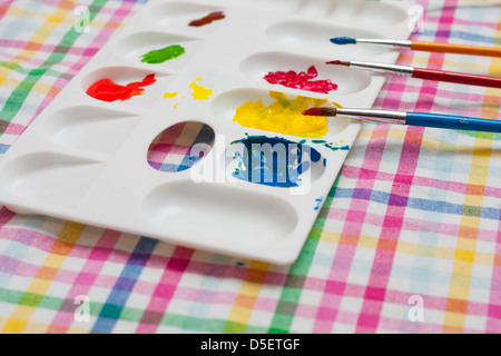 Palette mit Farben und Pinsel auf farbigen Hintergrund Stockfoto