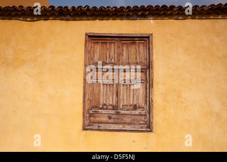 Alten hölzerne Fensterläden inmitten einer leuchtend gelben farbigen Wand in der alten Stadt Garachico, Teneriffa. Stockfoto