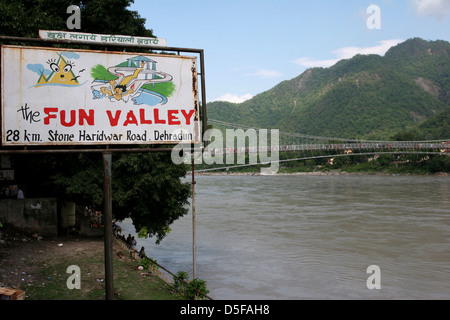 Ein Zeichen Werbung einen Vergnügungspark in der Nähe von Rishikesh, der Shibvanand Jhula Brücke über den Ganges im Hintergrund. Stockfoto