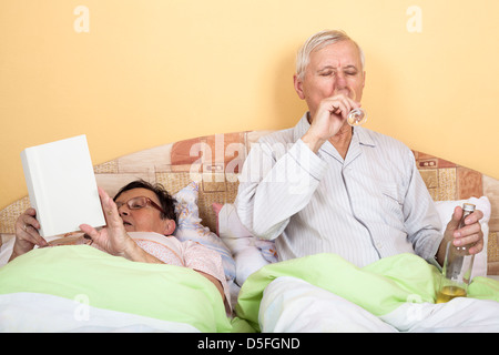 Ältere Menschen trinken Alkohol und Frau liest Buch im Bett Stockfoto