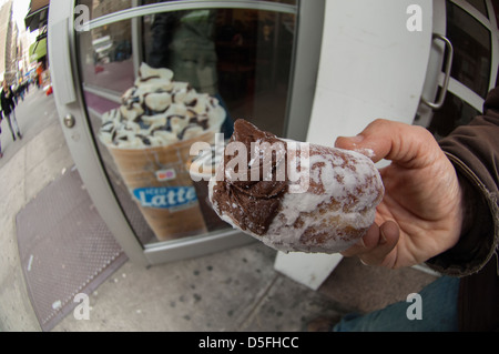 Eine Person hält einen Puderzucker Schokolade Creme Donut außerhalb einer Dunkin Donuts Filiale in Chelsea in New York Stockfoto