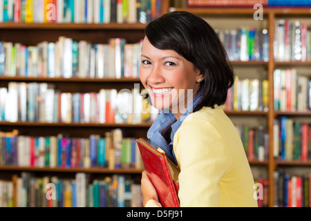 Student - eine junge asiatische Frau oder Mädchen lernen in einer Bibliothek stolz hält sie ein Buch oder ein Lehrbuch Stockfoto