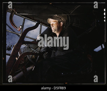 Ein Kranführer am Douglas Dam in Tennessee arbeitet in den 1940er Jahren Dieses Bild von Alfred T. Palmer zeigt die industrielle Szene mit dem Fokus des Bedieners auf Maschinen. Das Foto zeigt die Arbeitskräfte während des Zweiten Weltkriegs und das Projekt für öffentliche Arbeiten der Tennessee Valley Authority. Der Fahrer mit Kappe und Handschuhen betreibt einen großen Kran in einem dramatischen Himmel, der die industriellen Anstrengungen während des Krieges symbolisiert. Stockfoto