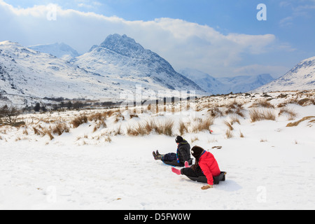 Kinder Rodeln in Bergen des Snowdonia National Park bei kaltem Wetter und Schneefall. Ogwen Valley, North Wales, UK Stockfoto