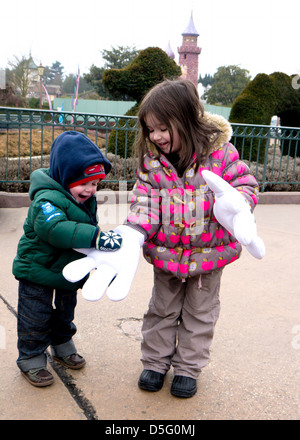 Ein Kleinkind schlägt die Hand von seiner großen Schwester, der über große Mickey mouse Handschuhe auf ihren Händen im Disneyland Paris trägt. Stockfoto