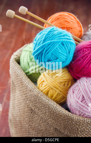 Wollene Kugeln aus Garn und hölzernen Stricknadeln in einer rustikalen Handwerk Tasche auf roten alten hölzernen Hintergrund Stockfoto