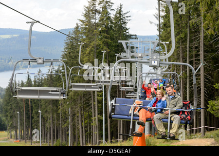 Junge Leute sitzen auf Sesselbahn geht durch Wald winken Stockfoto