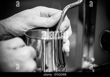 Ein paar Herren Hände dampfenden Milch in einen Krug für einen Espresso trinken Stockfoto