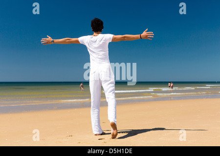 Gut aussehender Mann am Strand und Meer genießen seine Sommerferien, Arme ausgestreckt auf die Sonne als Symbol der Freiheit Stockfoto
