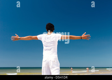 Gut aussehender Mann am Strand und Meer genießen seine Sommerferien, Arme ausgestreckt auf die Sonne als Symbol der Freiheit Stockfoto