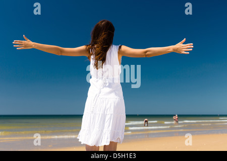 Hübsche Frau am Strand und Meer genießen ihre Sommerferien, Arme ausgestreckt auf die Sonne als Symbol der Freiheit Stockfoto
