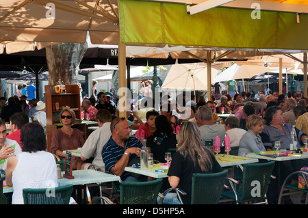 Touristen und Urlauber sitzen an Tischen im Freien ein Café in einem Stadtplatz in Südfrankreich. Stockfoto