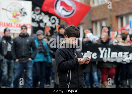 Demonstranten mit einem Banner besuchen die Demonstration Mölln 92, während ein Junge eine portable Videospiel im Stadt Zentrum von Mölln, Deutschland, 17. November 2012 spielt. Die Proteste März gliedert sich in Erinnerung von drei Opfern des Rechtsextremismus im Jahr 1992. Foto: Malte Christen Stockfoto