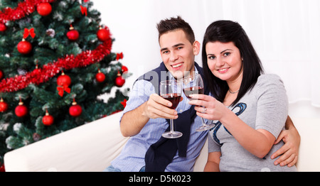 Freudige paar Toasten mit Wein und sitzen auf weiße Couch in der Nähe von Christmas tree Stockfoto