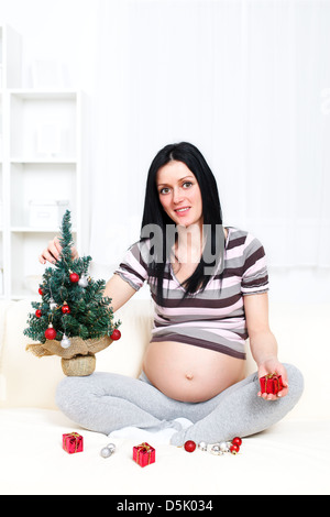 Foto einer glücklich schwanger Frau hält einen kleinen Weihnachtsbaum und kleine präsentiert Stockfoto