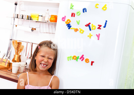 Kleines Mädchen lustiges Gesicht vor dem Kühlraum mit Farbe Brief Magnete zu Stockfoto