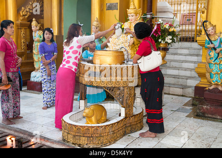 Anbeter gießt Wasser auf eine religiöse Statue an der Shwedagon-Pagode, Yangon (Rangoon), Myanmar (Burma) Stockfoto