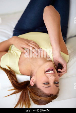Junge Frau auf dem Bett liegend und mit Handy Stockfoto