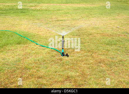 Wasser Sprinkler. Bewässerungs-System - Technik der Bewässerung im Garten. Rasensprenger Sprühwasser über grünen Rasen. Stockfoto