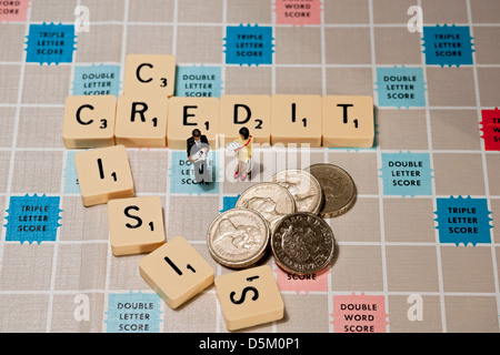 Fliesen auf dem Scrabble-Brett, die Kreditkrise schreiben, mit Spielzeugmann und -Frau und englischem Geld-Pfund-Münzen Bargeld-Rezession-Business-Finanzierungskonzept Stockfoto