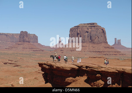Blauer Himmelsblick auf Merrick & West Mitten Buttes, Touristen & Mann sitzen Cowboy Pferd, John Ford Point, Monument Valley, Arizona Stockfoto