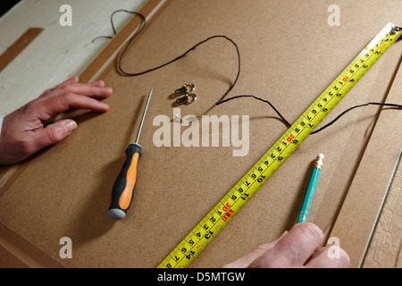 Messung der Band Schraubendreher hängenden Fäden und Befestigungen auf der Rückseite eines Bilderrahmens in einem Framing-workshop Stockfoto
