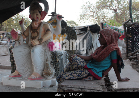 Eine indische Frau ruht neben einem lebensgroßen Idol der Hindu Gott Ganesh in der Ortschaft Gulbai Tekra von Ahmedabad, Gujarat, Indien. Stockfoto