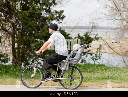 Ein junger Vater reitet sein Fahrrad mit seinem Sohn in einem Träger montiert. Radwege an Overholser See in Oklahoma City, Oklahoma, USA. Stockfoto