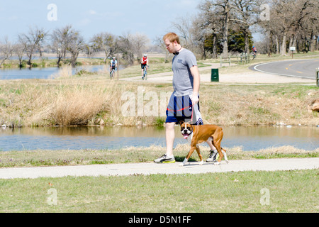 Ein rothaariger Junge geht seinen Boxer-Hund auf den Wanderwegen neben dem North Canadian River in Oklahoma City, Oklahoma, USA. Stockfoto