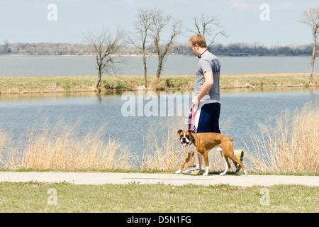 Ein rothaariger Junge geht seinen Boxer-Hund auf den Trails rund um Overholser See in Oklahoma City, Oklahoma, USA. Stockfoto