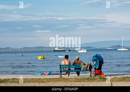 2 Freunde sitzen auf einer Bank am Meer warten auf Transport. Adria-Insel Susak-Kroatien. Stockfoto