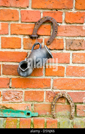 alte rote Ziegelsteine Mauer mit verrosteten Hufeisen und schwarzen Krug Stockfoto