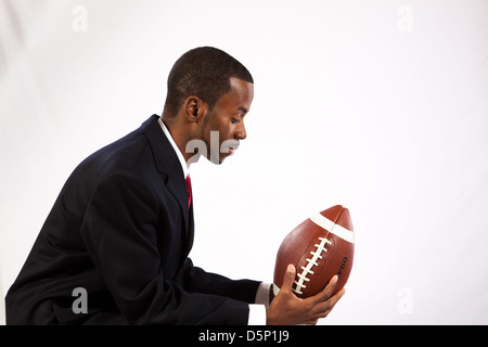 Schöner schwarzer Mann trägt einen dunklen Anzug, weißes Hemd und roter Krawatte, hielt ein American Football und Erinnerung an seine Jugend Stockfoto