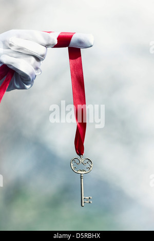 eine Hand in weißen Handschuhen hält einen alten Schlüssel auf einem roten Band Stockfoto