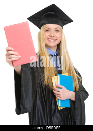 Lächelnde junge Frau in Graduierung Kleid zeigt Buch Stockfoto