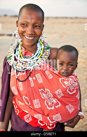 Afrika, Tansania; lächelnd von Massai-Frauen und Mutter mit 2 Babys im Arm in traditioneller Tracht mit Hand gemacht Schmuck Stockfoto