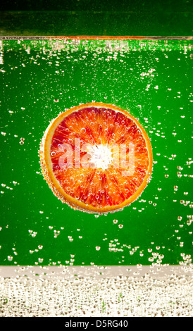 frische rote Orange fällt im Wasser auf einem grünen Hintergrund Stockfoto