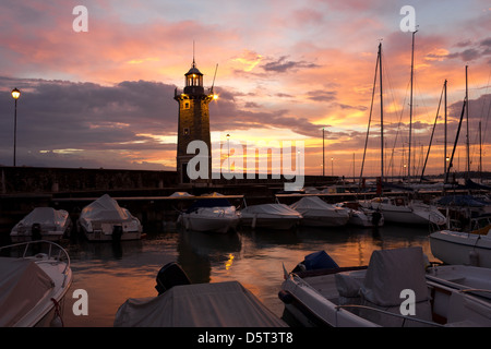 Bunte Sonnenaufgang in Desenzano del Garda in Italien mit den Booten in der Marina und dem alten Leuchtturm. Stockfoto