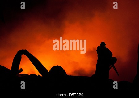 Silhouette der Feuerwehrleute kämpfen ein wütendes Feuer mit riesigen Flammen des brennenden Holzes Stockfoto