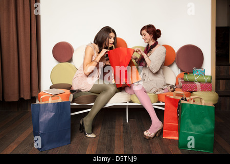 junge Mädchen sitzt auf einem schönen Sofa, umgeben von bunten Einkaufstüten Stockfoto