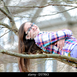 Eine schöne Teenager-Mädchen auf den Ästen eines Baumes liegen. Stockfoto