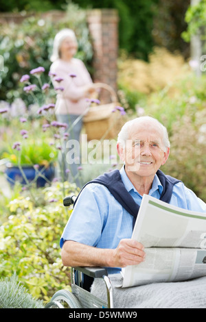 Älterer Mann im Rollstuhl Zeitunglesen im freien Stockfoto