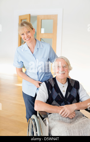 Pflegeperson älteren Mann im Rollstuhl schieben Stockfoto